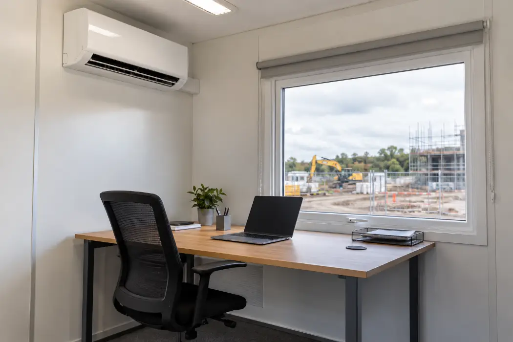 Wall-mounted air conditioning unit above a desk in a site cabin office